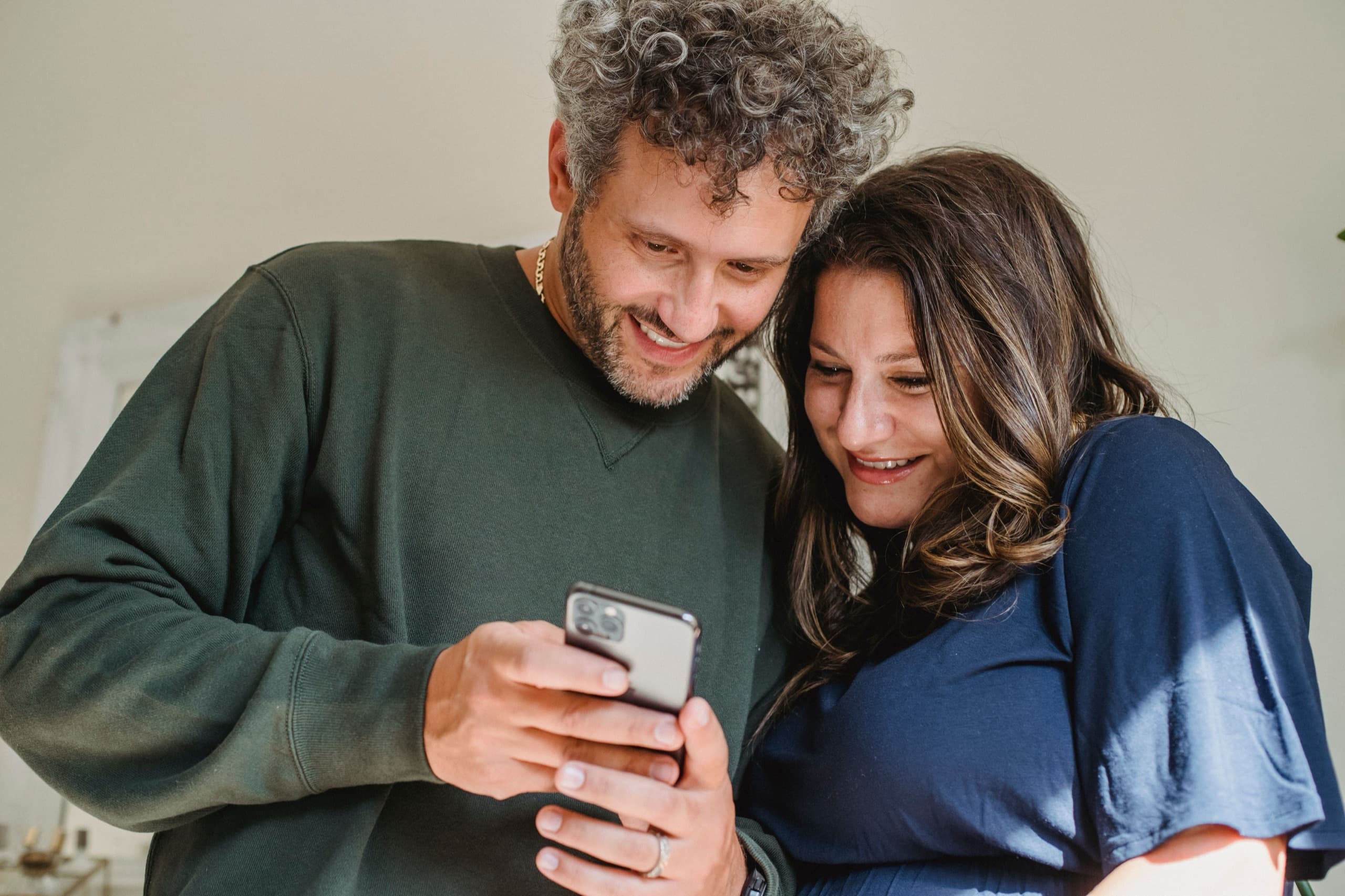 A couple smiling as they look at a phone together at home